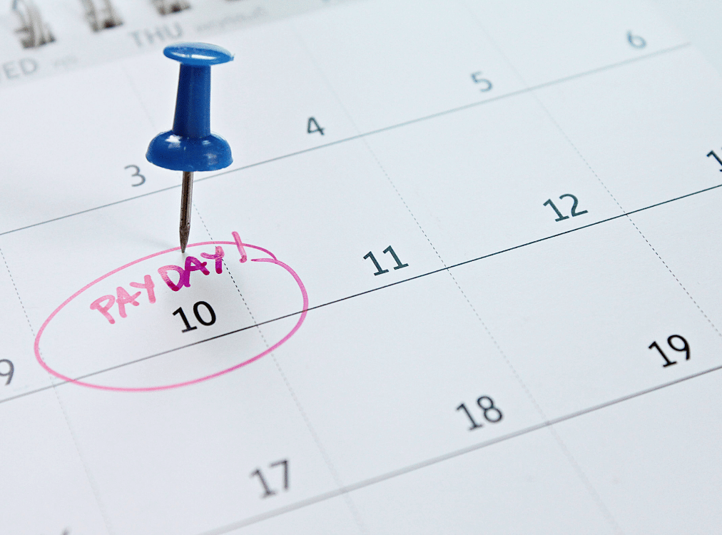 A blue pushpin marks the 10th on a calendar, with the date circled in pink and labeled "PAY DAY!. A blue pushpin marks the 10th on a calendar, with the date circled in pink and labeled "PAY DAY!.